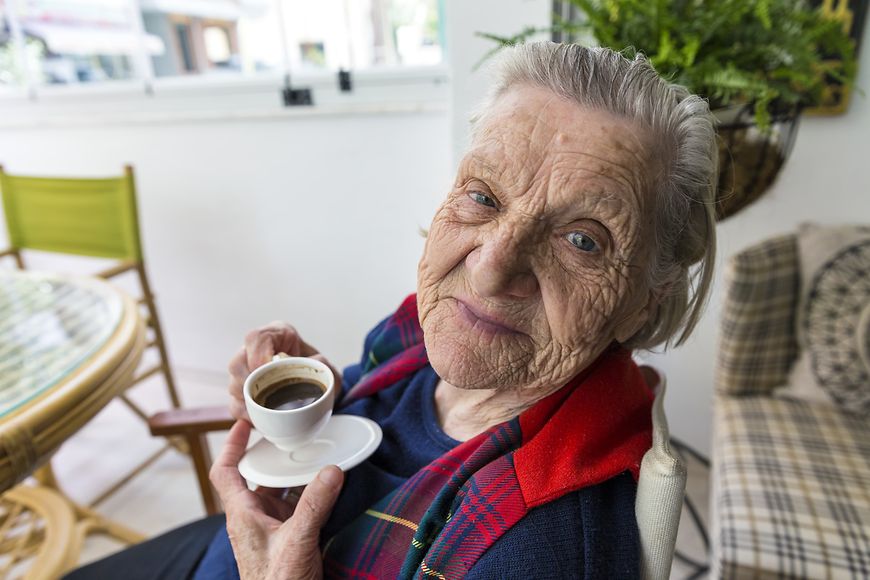 Alte Frau mit türkischem Kaffee in der Hand blickt direkt lächelnd in die Kamera
