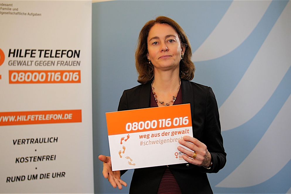 Bundesfrauenministerin Dr. Katarina Barley hält ein Schild mit der Nummer des Hilfetelefons in der Hand