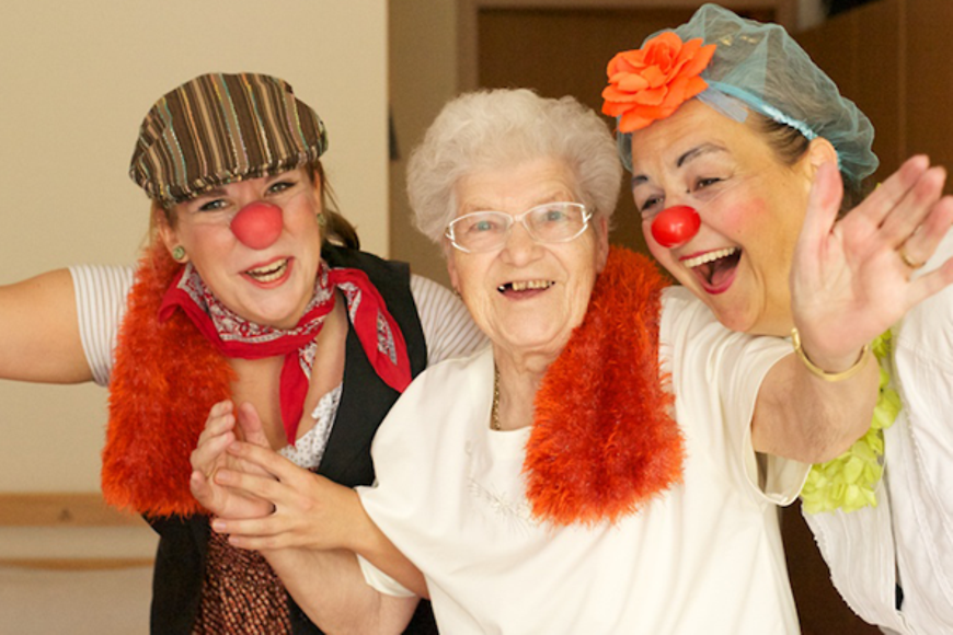 Zwei Clowns lachen gemeinsam mit einer alten Frau