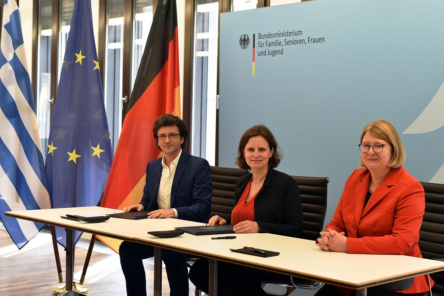 Juliane Seifert, Antje Leendertse und Pafsanias Papageorgiou am Tisch mit Vertragsunterlagen und Flaggen im Hintergrund