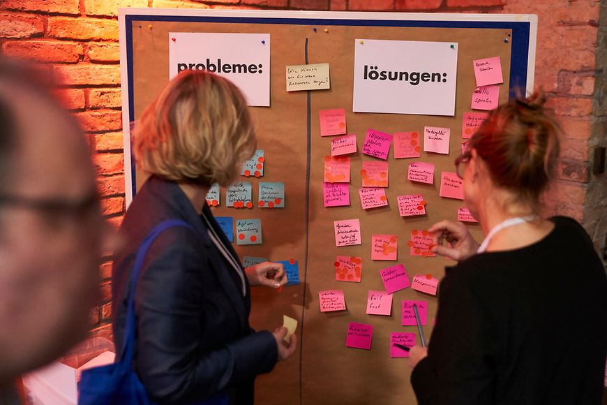 Zwei Frauen stehen beim Digital Social Summit 2019 an einer Wand mit Haftzetteln und den Überschriften "Probleme" und "Lösungen"