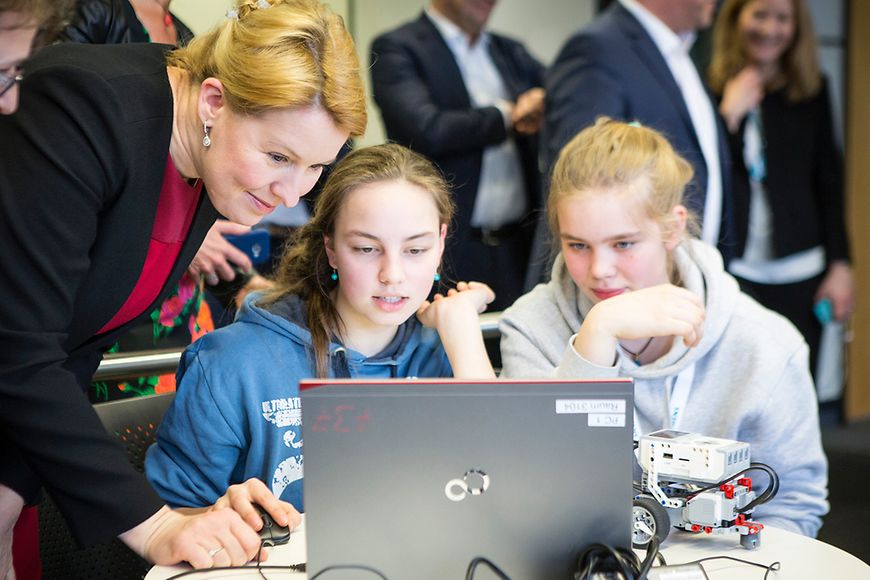 Zwei Mädchen schauen gemeinsam beim Girls'Day mit Dr. Franziska Giffey auf einen Laptop, neben dem ein Roboterfahrzeug steht