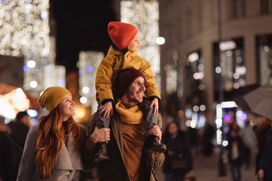 Eine junge Familie läuft durch eine weihnachtlich beleuchtete Stadt
