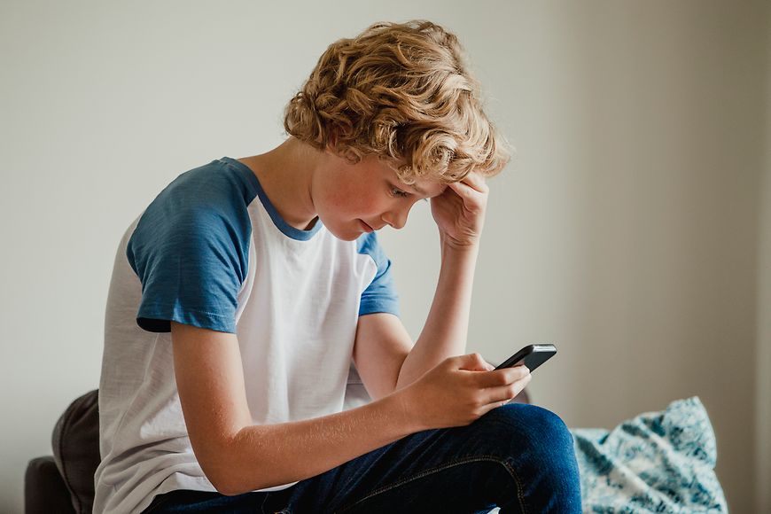 Ein Junge sitzt auf dem Bett und chattet auf seinem Handy