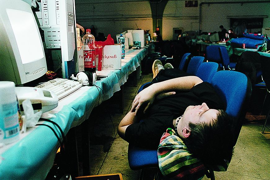Ein junger Mann liegt auf mehreren zusammengestellten Stühlen und schläft 