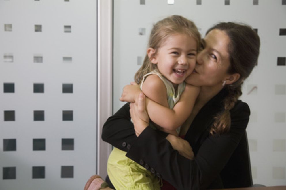Eine berufstätige Mutter gibt ihrer Tochter einen Kuss. 