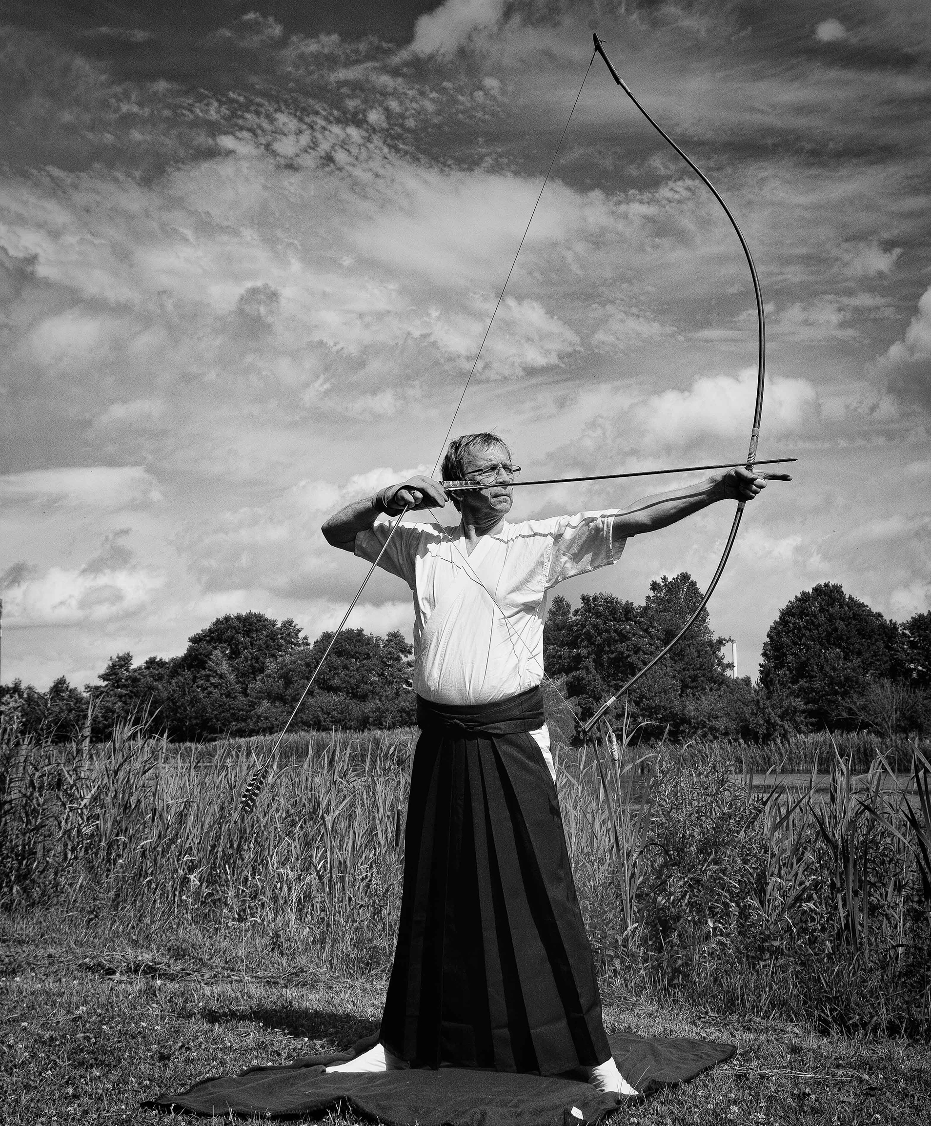 Älterer Mann spannt einen Bogen und hält einen Pfeil in der Hand