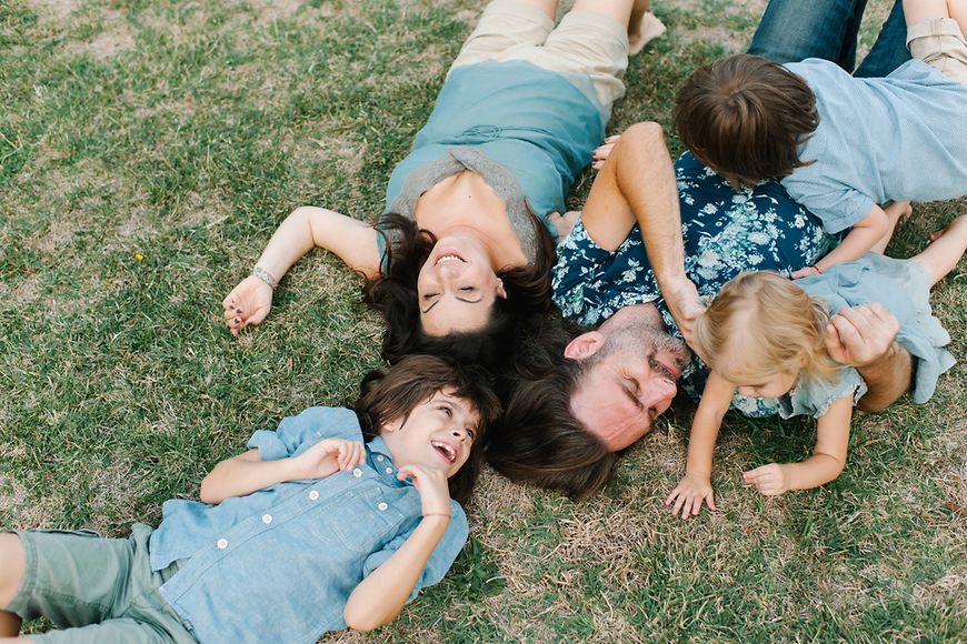 Mutter, Vater und drei Kinder spielen auf einer Wiese