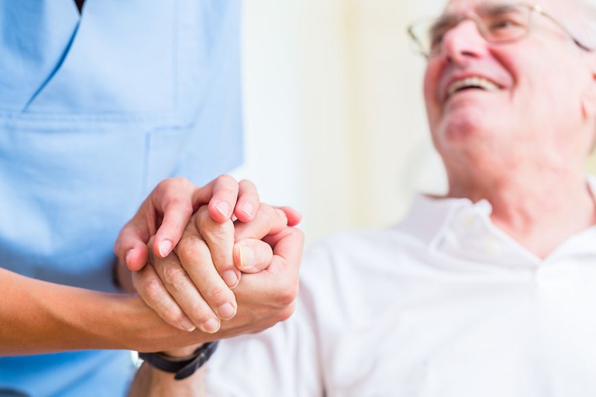 Ein Pfleger hält die Hand eines älteren Patienten