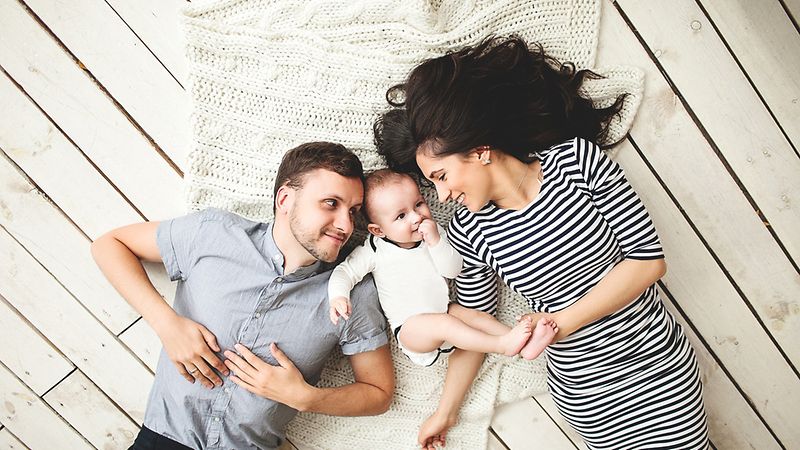 Eltern und Baby liegen auf dem Boden und lachen 
