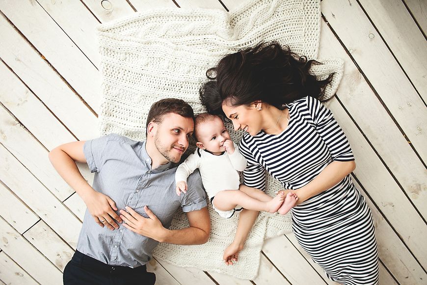 Eltern und Baby liegen auf dem Boden und lachen 