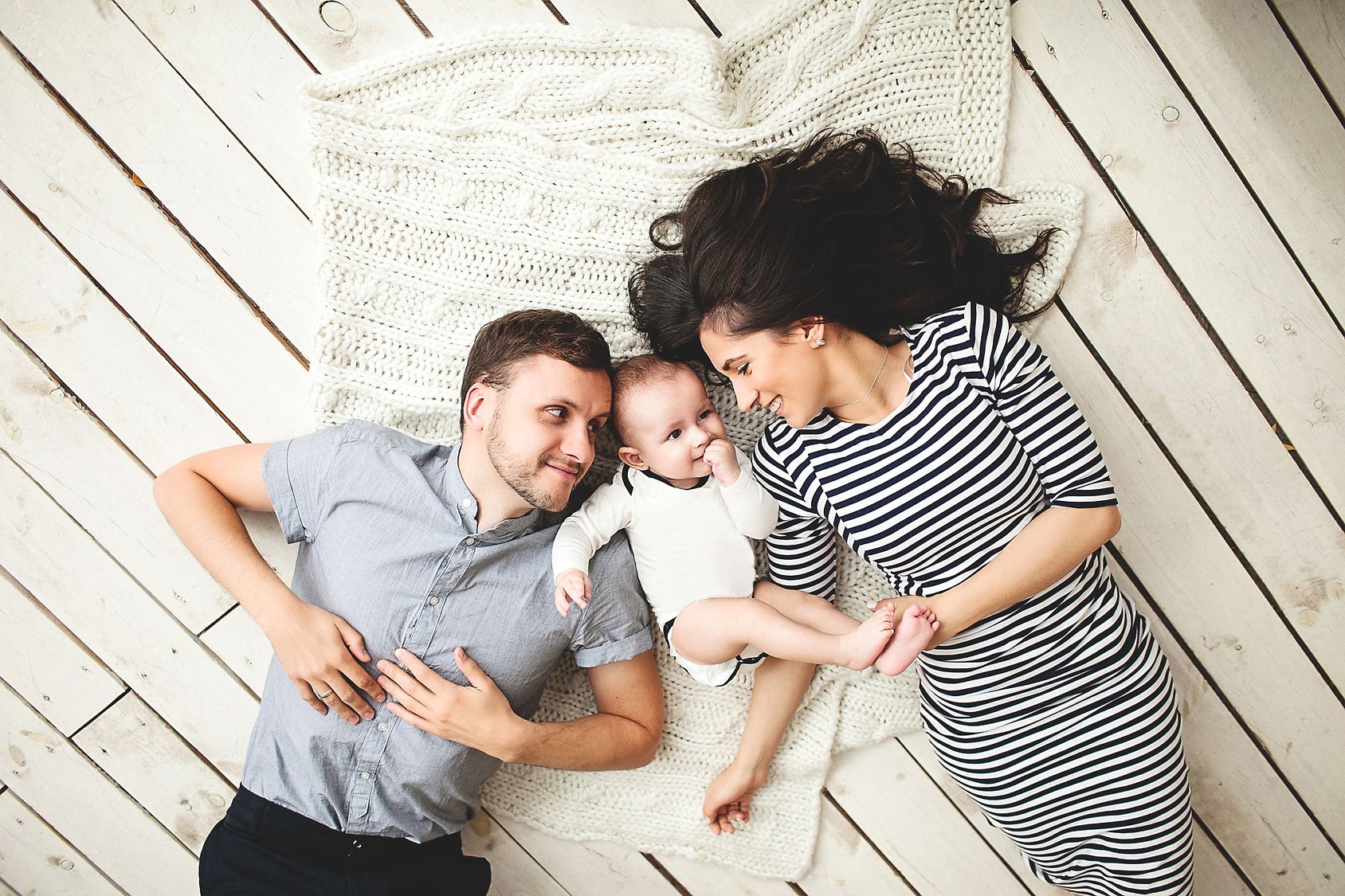 Eltern und Baby liegen auf dem Boden und lachen 