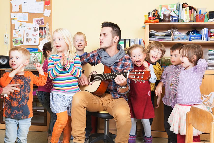 Erzieher spielt Gitarre und singt mit Kita-Kindern