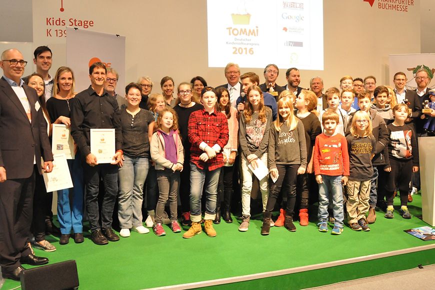 Dr. Ralf Kleindiek auf einer Bühne mit den Gewinnerinnen und Gewinnern des TOMMI-Preises