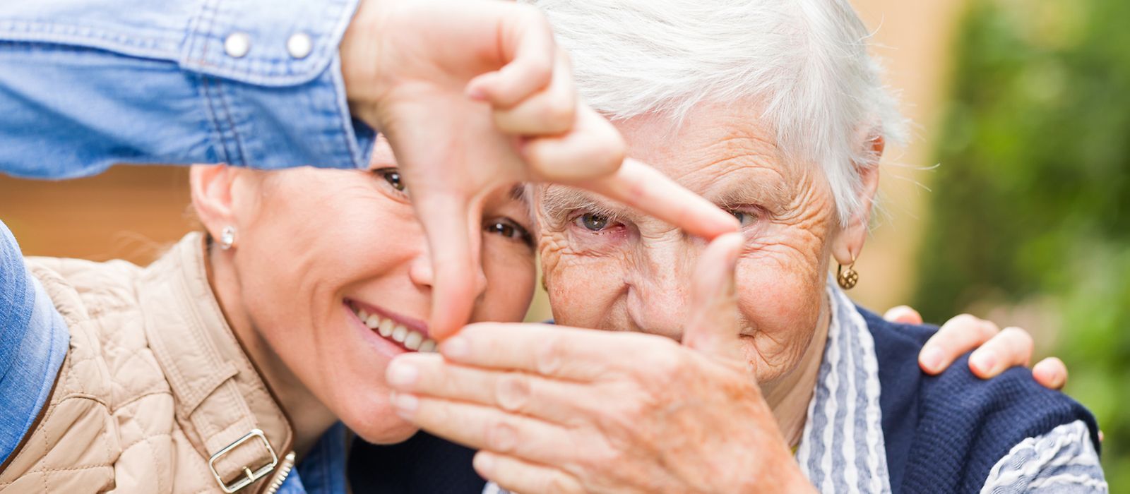 Eine junge und eine ältere Dame stehen lächelnd zusammen und halten mit den Händen ein Quadrat in die Fotokamera