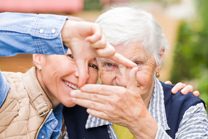 Eine junge und eine ältere Dame stehen lächelnd zusammen und halten mit den Händen ein Quadrat in die Fotokamera