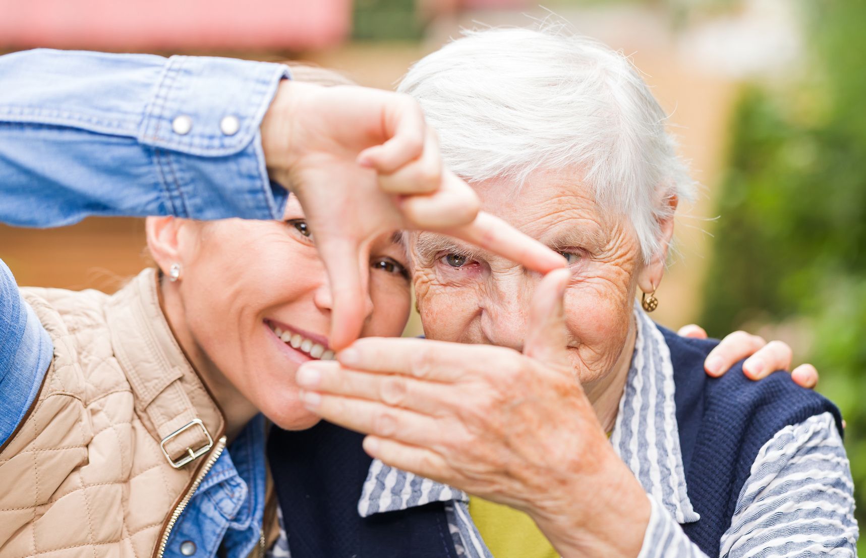 Eine junge und eine ältere Dame stehen lächelnd zusammen und halten mit den Händen ein Quadrat in die Fotokamera