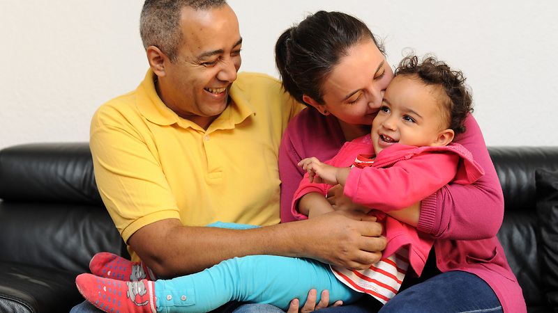 Mutter, Vater und Kind in liebevoller Umarmung auf eine Couc