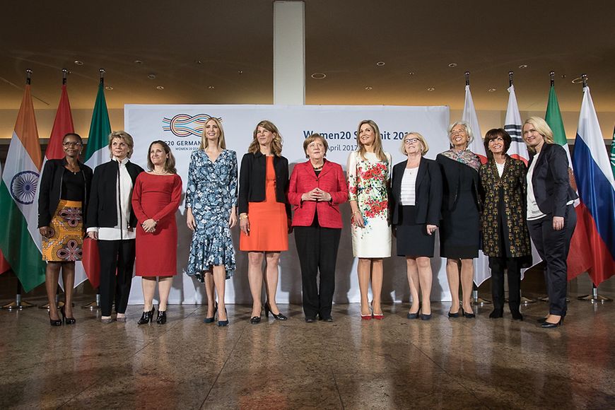 Angela Merkel mit zehn Regierungsvertreterinnen und eingelandenen Gästen beim W20-Gipfels, im Hintergund Flaggen