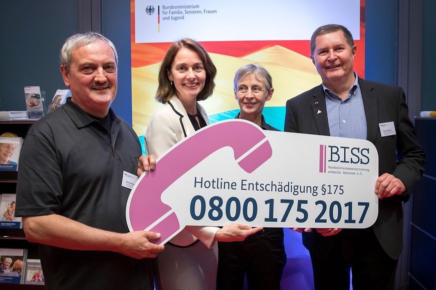 Dr. Katarina Barley und drei Mitarbeitende des BISS halten gemeinsam ein Schild mit der Entschädigungshotline in den Händen