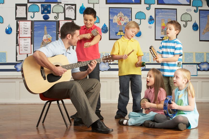 Mann spielt Gitarre, Gruppe von Kindern musiziert mit ihm