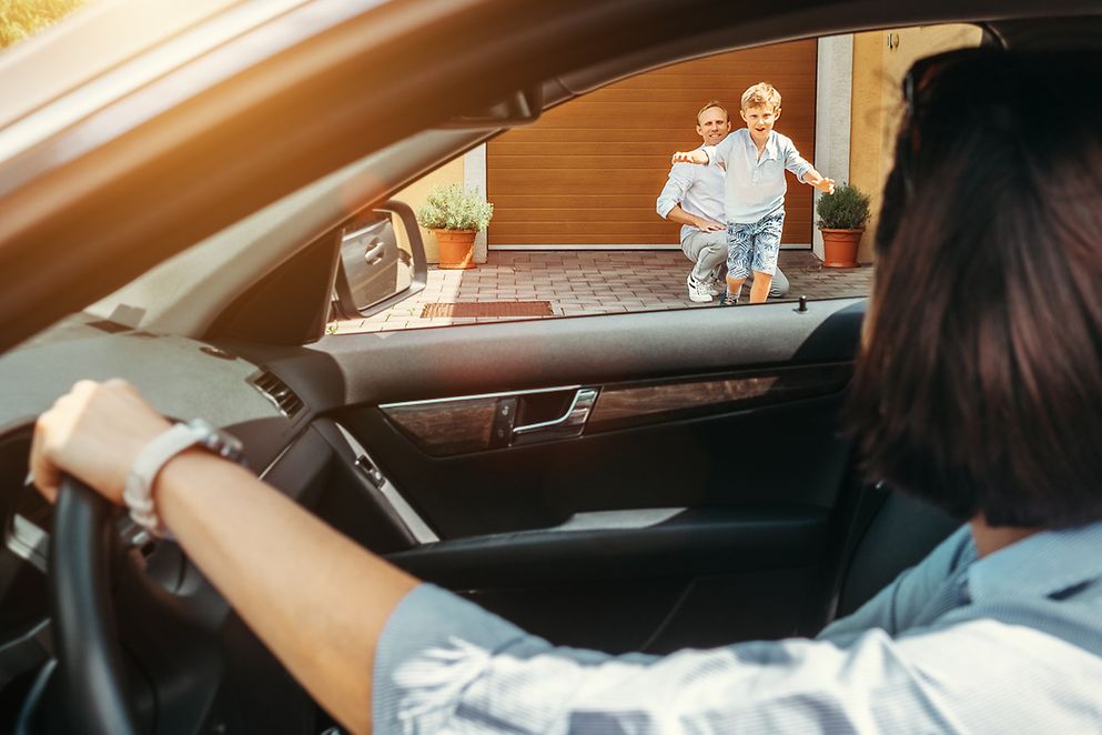 Mutter sitzt im Auto, Sohn läuft auf sie zu, Vater im Hintergrund