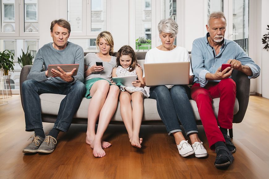 Eine Familie sitzt mit diversen mobilen Endgeräten wie Handys und Tablets gemeinsam auf der Couch