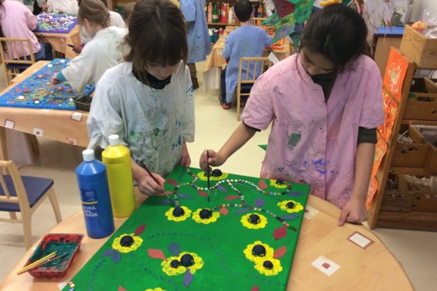 Zwei Mädchen in Malerkitteln malen zusammen ein Bild mit Sonnenblumen