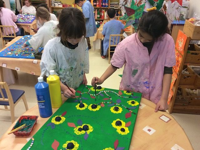 Zwei Mädchen in Malerkitteln malen zusammen ein Bild mit Sonnenblumen
