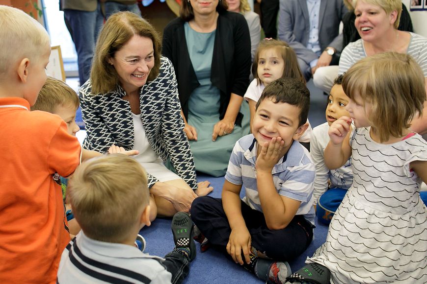 Die Bundesfamilienministerin sitzt mit Kindern auf dem Boden und lacht