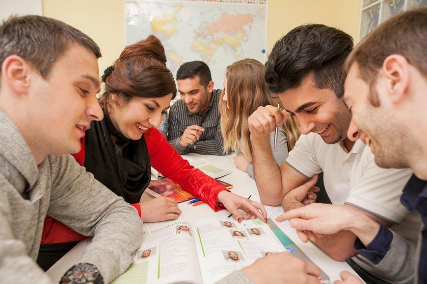 Junge Frauen und Männer sitzen an einem Tisch und bearbeiten gemeinsam eine Aufgabe