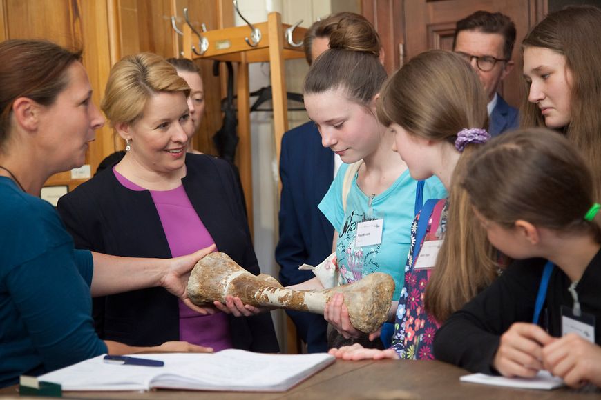 Dr. Franziska Giffey schaut einen Dinosaurierknochen an, den eine Schülerin in der Hand hält