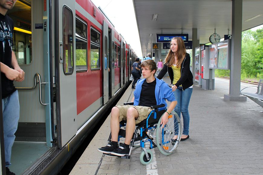 Ein junger Rollstuhlfahrer und seine Begleitung besteigen einen Zug