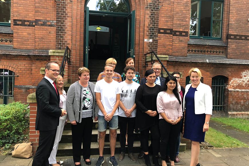 Die Ministerin steht mit Schülerinnen, Schülern und Lehrenden der Alice-Salomon-Schule vor der Eingangstreppe