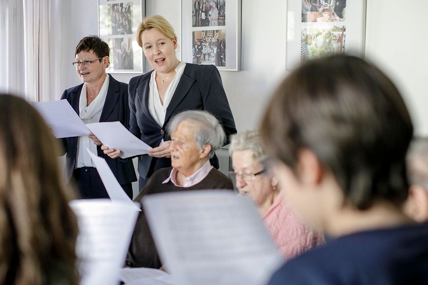 Das Bild zeigt Dr. Franziska Giffey mit mehreren älteren Menschen, die im Stuhlkreis sitzen und singen