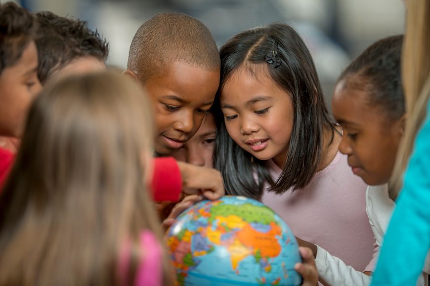 Kinder verschiedener Herkunft spielen mit einem Globus