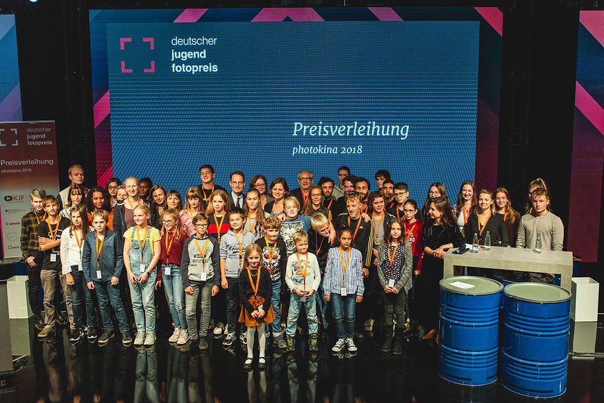 Das Bild zeigt Juliane Seifert mit allen Preisträgerinnen und Preisträgern vor einer Fotowand der photokina