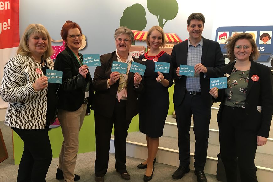 Das Bild zeigt eine Gruppe, die Schilder mit der Aufschrift "Selbst ist die Frau" halten