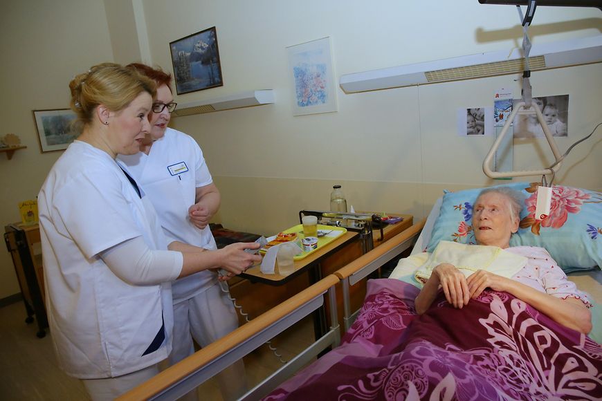 Das Bild zeigt Franziska Giffey und eine Pflegerin am Bett einer alten Dame