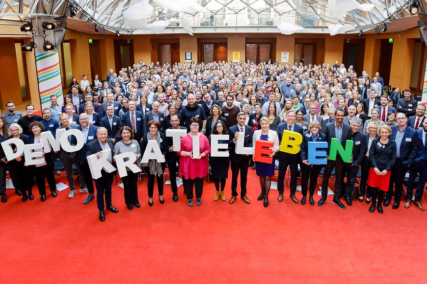 Das Bild zeigt ein Gruppenbild mit Menschen und dem Schriftzug "Demokratie leben"