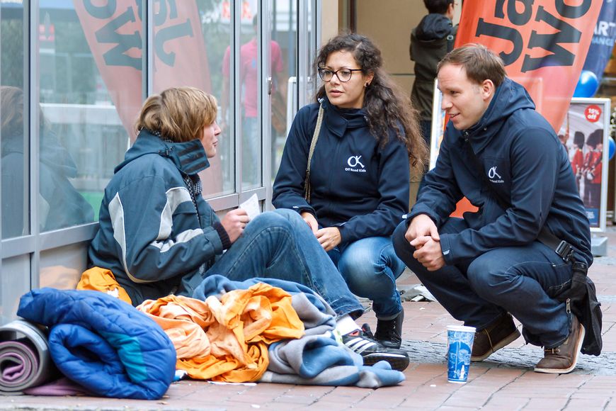 Das Bild zeigt ein Straßenkind mit zwei Streetworkern, die mit ihm reden