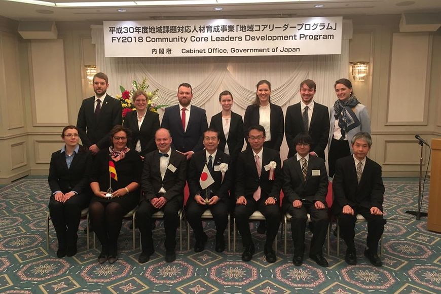 Eine Gruppe mit Vertretern aus Deutschland und Japan steht und sitzt in zwei Reihen vor einem Banner des Forums in Japan