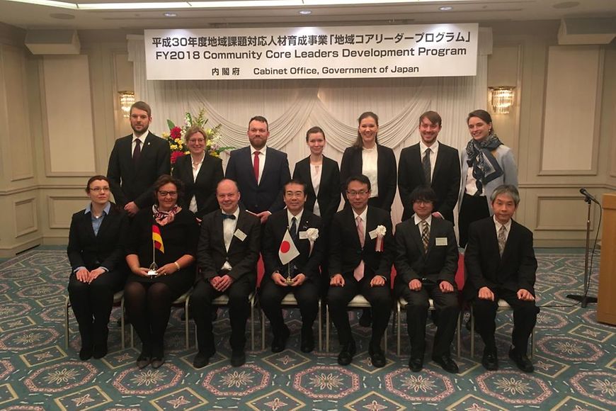 Eine Gruppe mit Vertretern aus Deutschland und Japan steht und sitzt in zwei Reihen vor einem Banner des Forums in Japan