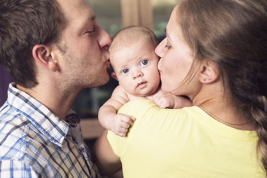 Das Bild zeigt Eltern, die ihr Baby küssen