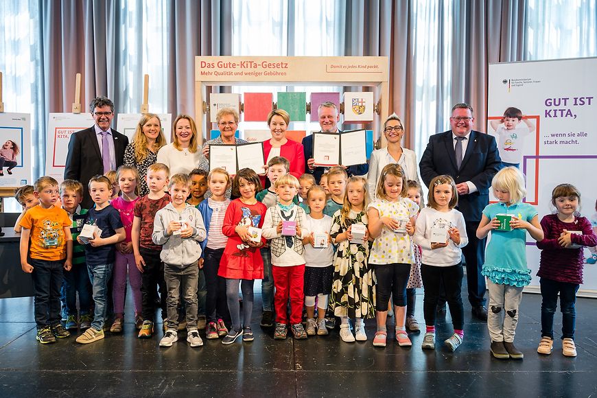 Franziska Giffey, Ulrich Commerçon in einer Gruppe mit vielen Kindern vor Aufstellern zum Gute-Kita-Gesetz