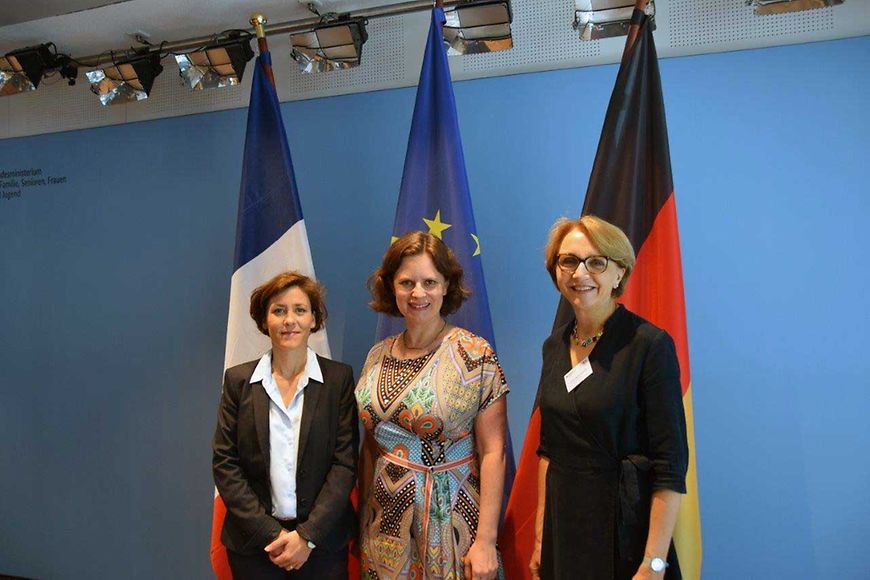 Das Bild zeigt Juliane Seifert mit zwei Damen vor einer deutschen, einer französischen und europäischen Flagge
