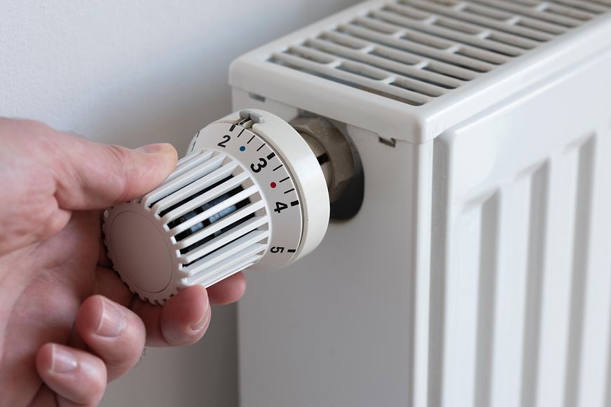Nahaufnahme einer Person, die den Thermostat an der Heizung herunter dreht, um Energie zu sparen.