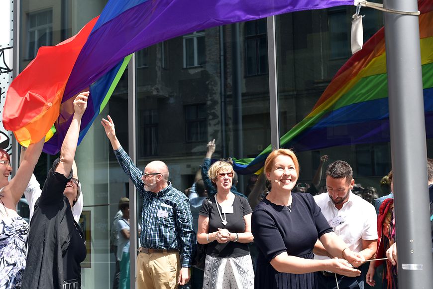 Dr. Franziska Giffey hisst die Regenbogenflagge zusammen mit vielen Menschen vor dem Bundesfamilienministerium