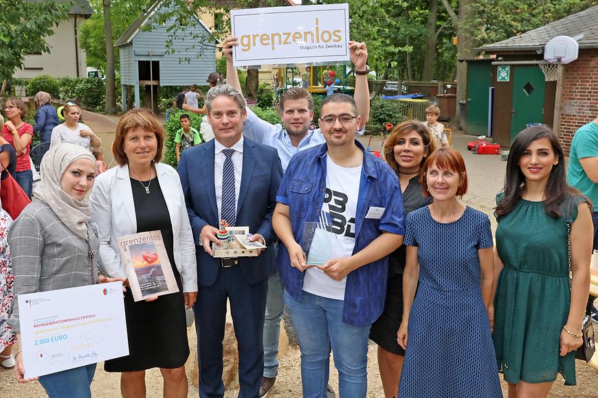 Eine Gruppe von Menschen im Garten des Mehrgenerationenhauses Zwickau mit einem Scheck und dem Cover des Magazins grenzenlos