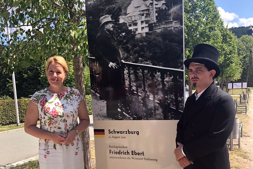 Dr. Franziska Giffey und ein Mann mit Spitzbart und Zylinder vor einem Bild von Friedrich Ebert vor der Schwarzburg von 1919